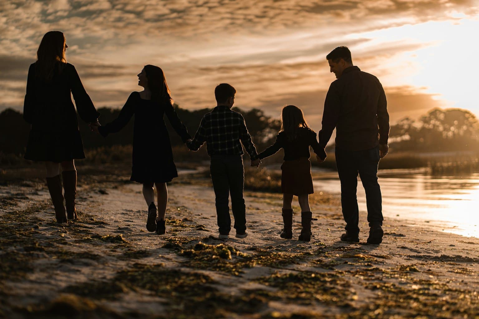 A multi-generational family walking hand-in-hand on the beach at sunset.